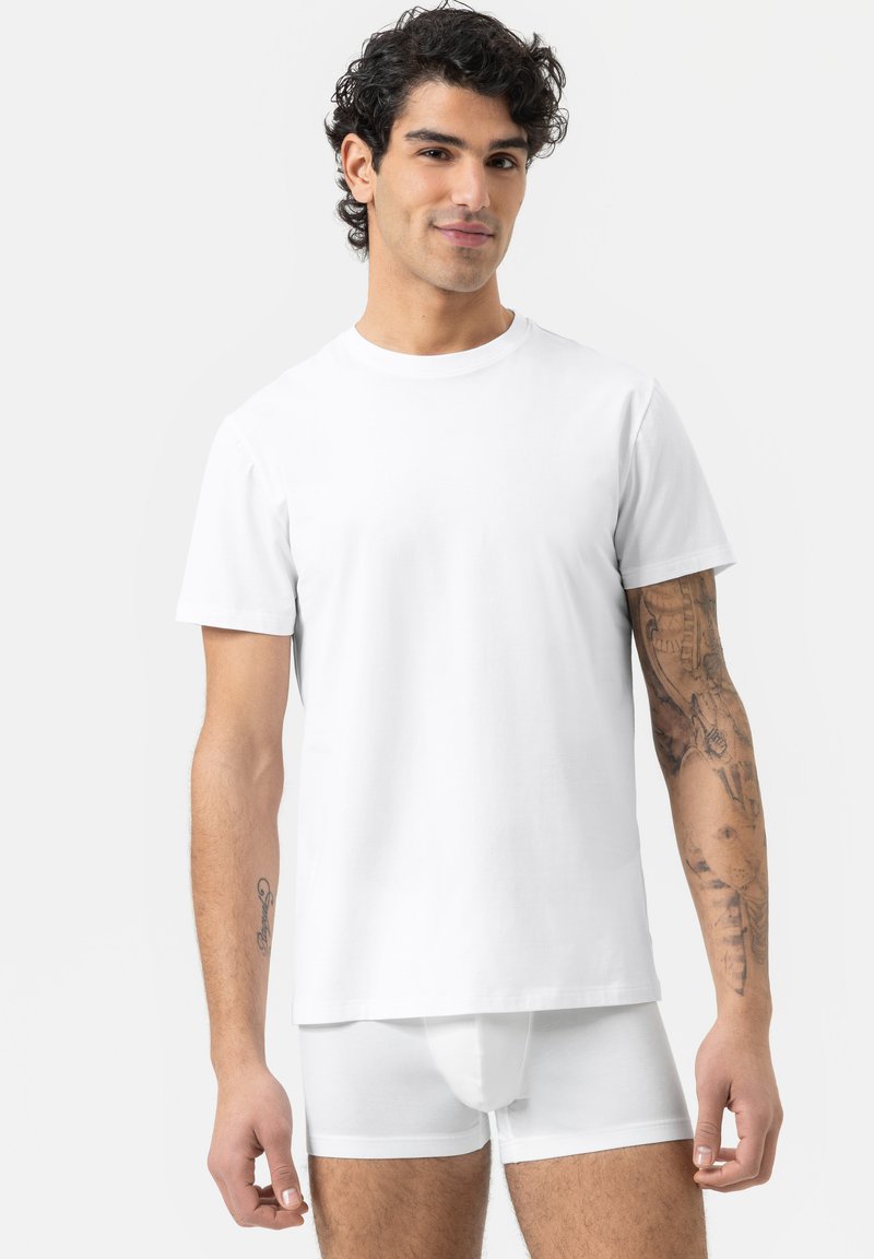 T-shirt en coton blanc à manches courtes, col rond et coupe décontractée. Porté avec un boxer blanc. Texture claire et lisse.