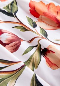 Tissu blanc avec de grands imprimés floraux rouges et orange ainsi que des feuilles vertes, montrant des détails fins et une texture douce.