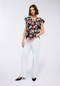 Blusa nera a fiori con fiori rosa, con maniche corte a volant, abbinata a pantaloni bianchi a gamba larga e décolleté neri a punta.