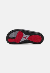 Black rubber sneaker sole with red and gray accents. Features textured grip patterns and a logo at the center.