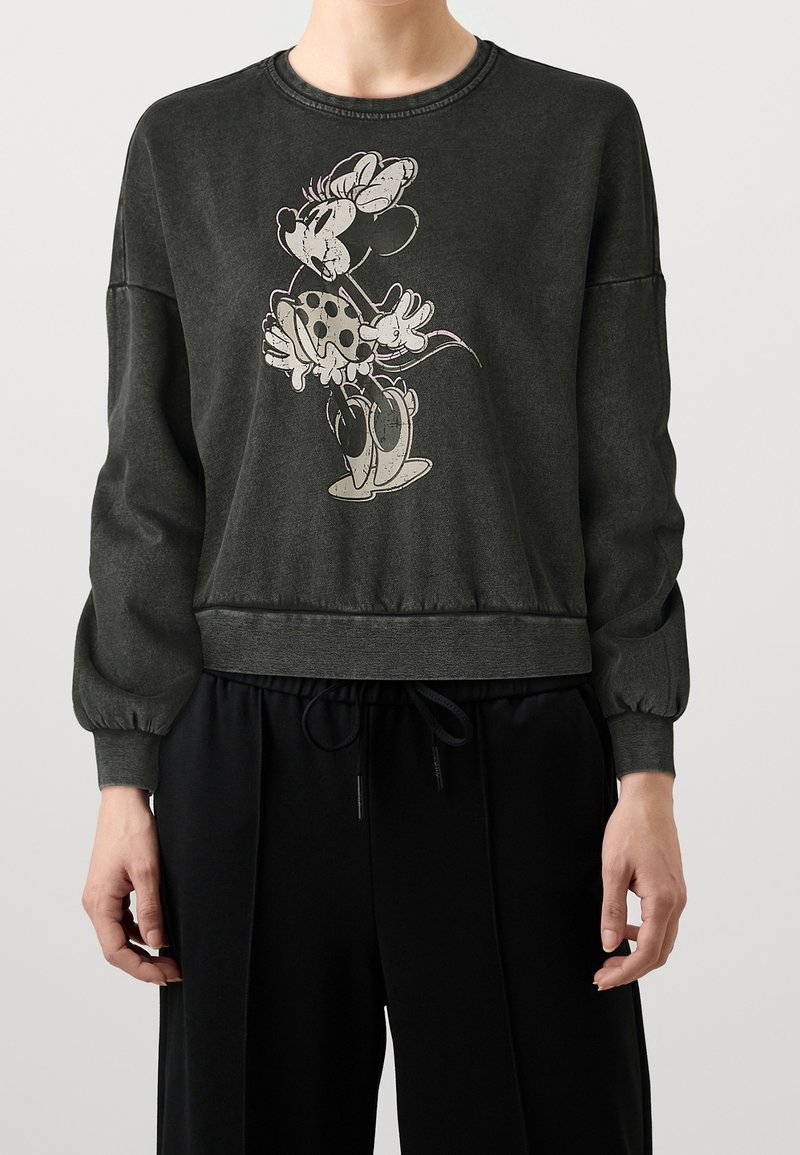 Sweat-shirt vert foncé avec manches longues bouffantes ornées d'un dessin d'un personnage tenant des fleurs. Bordures côtelées et coupe décontractée à la taille.