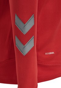 Rød atletisk skjorte med tekstureret stof, med grå chevronmønstre på ærmerne og "BEECOOL" logoet nederst.