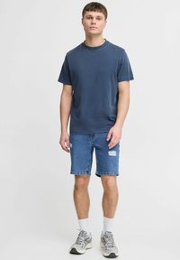Camiseta de algodón azul marino combinada con pantalones cortos de mezclilla azul claro con detalles desgastados. Llevado con calcetines blancos y zapatillas grises.