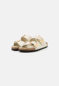 Beige sandalen met gouden gespen, kurken voetbed en zwarte rubberen zool. Twee verstelbare banden aan de bovenkant voor een stevige pasvorm.