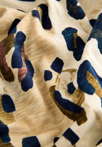 Tkanina z reliefno površino v kremni barvi z abstraktnimi temno modrimi, zelenimi in rjavimi oblikami. Gladek in lahek material z mehkim videzom.