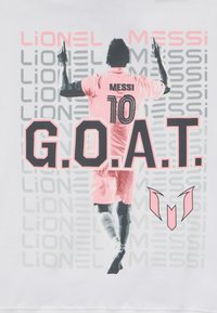 Biała koszulka z grafiką gracza w różowym, z napisem "MESSI" i numerem "10" na plecach oraz wyraźnym napisem "G.O.A.T.".