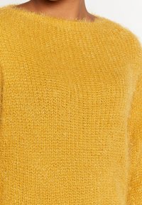 Gul stickad tröja gjord av mjukt, fluffigt material, med en lös passform och vid halsringning, samt en texturerad yta.
