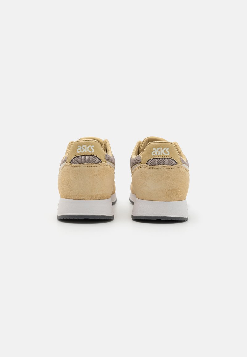 Zapatillas de ante beige claro con parte superior de malla, detalles en gris y una media suela blanca. Presenta un logo en el talón y una suela texturizada.