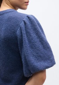 Blue wool sweater with a soft texture, featuring voluminous puff sleeves and a classic round neckline. Close-up of shoulder detail.