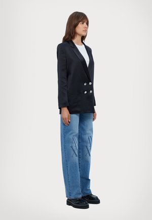 Svart dobbeltradet blazer med sølvknapper, matchet med lyseblå vide jeans med logo print, og kraftige sorte sko.