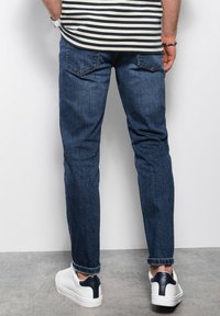 Jean en denim bleu foncé avec une coupe slim, dotés de poches arrière et de bas de pantalon retroussés, associés à des baskets blanches avec un accent marine.