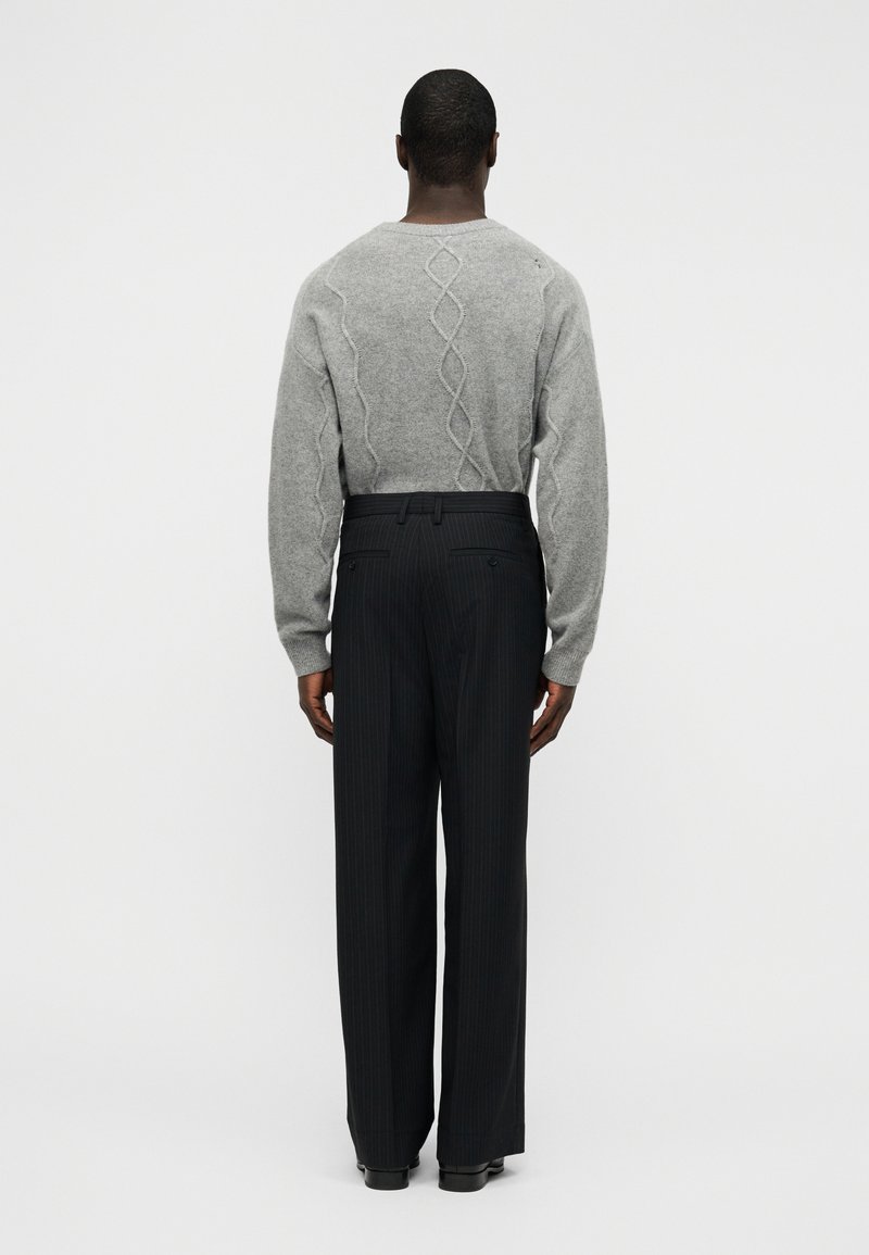 Gray knitted sweater with a twisted cable design at the back, paired with black pinstriped trousers, showing a relaxed fit.