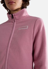 Roze fleece zip-up jack met een hoge kraag, met een wit merkimago op de borst, een soepele textuur en een getailleerd silhouet.