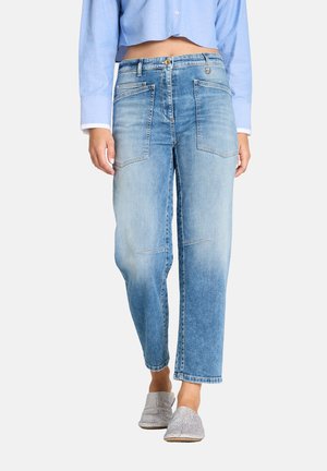 Persoon draagt een lichtblauw cropped overhemd met knopen en lichtblauwe high-waist jeans met grote voorzakken en glinsterende slip-on schoenen.