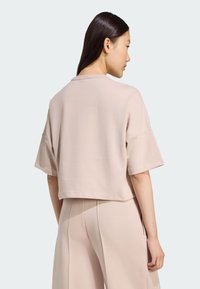 Skraćena svijetlosiva dukserica kratkih rukava, od mekog materijala, s jednostavnim izrezom. Uparena s odgovarajućim hlačama za usklađeni izgled.