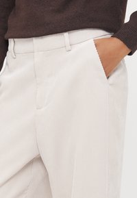Pantalon en velours côtelé beige clair avec des rayures verticales, doté de poches latérales et d'une coupe droite. Le tissu texturé ajoute un intérêt visuel.