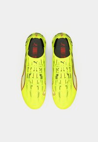 Neongule fodboldsko med tekstureret overdel, røde accenter og sort indersål. Har stribet design og snørebånd for sikker pasform.