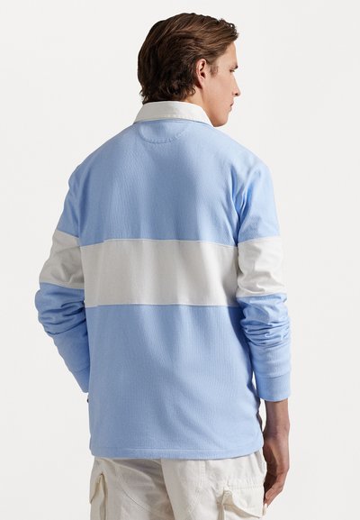 Gaiši zila garām piedurknēm polo krekls ar baltu horizontālu joslu. Mīksta tekstūra, ribotas piedurknes un apkakles detaļa redzama no aizmugures.