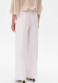 Wijde broek van zacht wit materiaal met een gladde textuur. Elastische tailleband voor comfort. Licht verborgen zoom en subtiele draping.