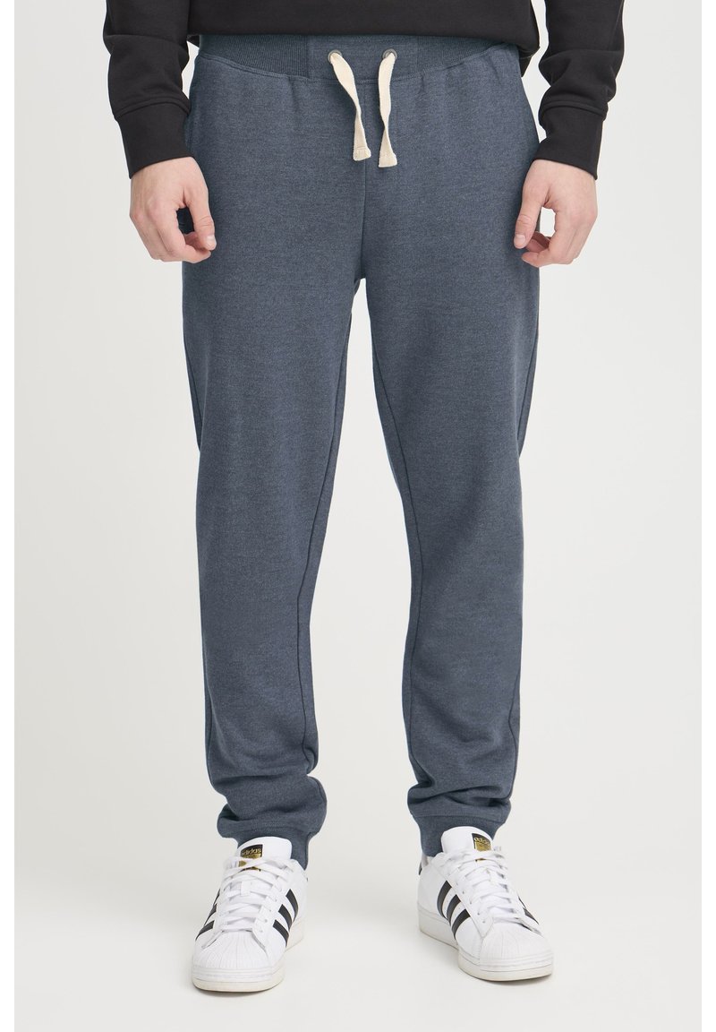 Marineblå sweatpants lavet af blødt stof med en snøre i taljen, sidelommer og et tapered ben design. Kombineret med hvide sneakers.