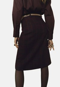 Bordeaux geruite rok met een rechte snit, gecombineerd met een donkerbruine blouse. Metaal hardware riem en getextureerde panty zichtbaar.