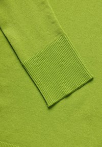 Tessuto di maglione a maglia verde con dettagli a costina ai polsini. Texture liscia, motivo di punto uniforme e colore vivace sono caratteristiche prominenti.