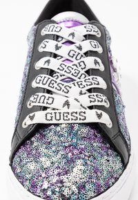 Sneaker nera con paillettes multicolori, caratterizzata da lacci con logo bianco e un accento viola. Texture liscia con decorazioni lucide.