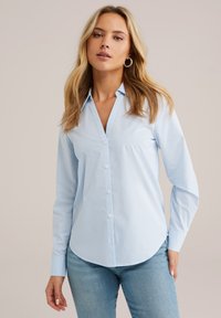 Lichtblauw gestreept shirt met een knoopsluiting aan de voorkant, lange mouwen en een gebogen zoom. De stof lijkt glad en lichtgewicht te zijn.