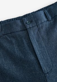 Pantaloni in denim scuro con chiusura a bottone, dotati di una cintura cucita e una texture liscia. Il tessuto presenta sottili motivi di tessitura.