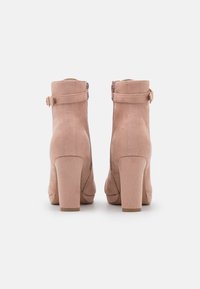 Stivaletti alla caviglia in suede rosa con punta rotonda, zip laterale e tacco spesso. Presentano una fascia con fibbia alla caviglia.