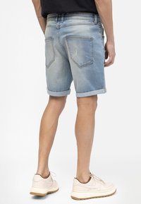 Hellblaue Jeansshorts mit umgeschlagenen Säumen, ausgestattet mit zwei Gesäßtaschen und leichter Abnutzung. Getragen mit beigen Turnschuhen.