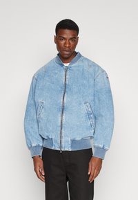 Ανοιχτό μπλε τζάκετ bomber από τζιν με μπροστινό φερμουάρ, ριμπ μανσέτες και ζώνη. Διαθέτει πλαϊνές τσέπες και μινιμαλιστικές ραφές.