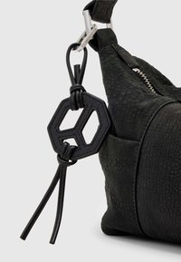 Primo piano di una borsa in pelle nera texturizzata con un ornamento in pelle esagonale legato a una fibbia in metallo argento sulla tracolla.