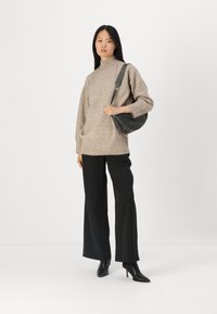Beige kötött pulóver magas nyakkal, fekete bő szárú nadrággal és fekete bokacsizmával párosítva. A modellen egy szürke keresztpántos táska látható.