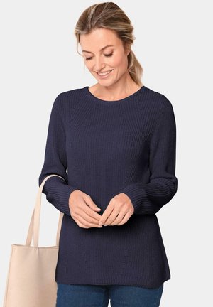 Marine gebreide trui met een ronde hals, geribbelde mouwen en naaddetails, gecombineerd met een lichtbeige tote bag.