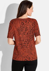 Korte mouwen top in levendig rood met een zwart dierenprint patroon. Heeft een ontspannen pasvorm en een ronde halslijn.