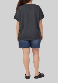 Losse, donkergrijze t-shirt met korte mouwen, gecombineerd met blauwe denim shorts. Zwarte instap schoenen maken de outfit compleet.