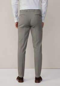 Grau maßgeschneiderte Hose mit glatter, leichter Textur. Verfügt über zwei Gesäßtaschen mit Knopfverschlüssen und einer schmalen Passform. Getragen mit braunen Schuhen.