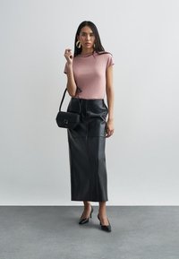 Różowy dopasowany t-shirt, czarna skórzana długa spódnica, mała czarna torebka i czarne szpilki z ostrym noskiem. Złote kolczyki koła dodają detalu. Gładkie tekstury.