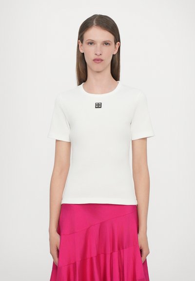 T-shirt bianco a maniche corte con costine, caratterizzato da un logo quadrato nero sul petto; abbinato a una gonna rosa fluida per creare contrasto.