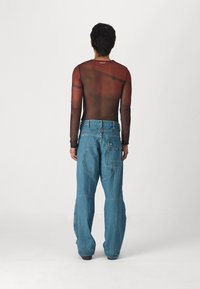 Top castanho semi-transparente de manga longa com um design ajustado e tons avermelhados em contraste, combinado com jeans de ganga azul largos com costuras únicas.