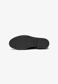 Suela de zapato de goma negra con patrón de textura, que presenta un diseño de agarre profundo y un corte rectangular cerca del talón.