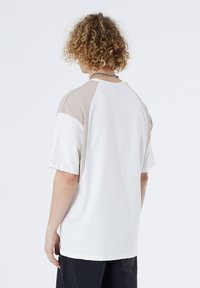 White t-shirt with beige raglan sleeves, featuring a loose fit and short sleeves. Made of soft cotton, suitable for casual wear.
