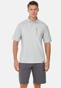 Polo shirt grigio chiaro con colletto, maniche corte e taschino con zip sul petto dotato di una zip arancione; abbinato a pantaloni corti grigi.