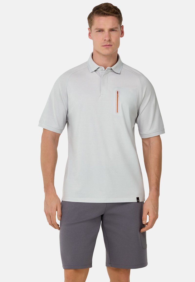 Polo shirt grigio chiaro con colletto, maniche corte e taschino con zip sul petto dotato di una zip arancione; abbinato a pantaloni corti grigi.