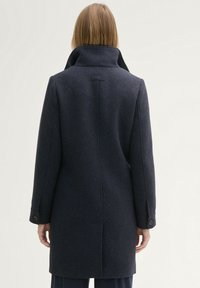 Tengerészkék gyapjú kabát magas gallérral, hosszú ujjal és gombos díszítéssel a mandzsettákon. Sleek, testhezálló hátrész designnal rendelkezik.