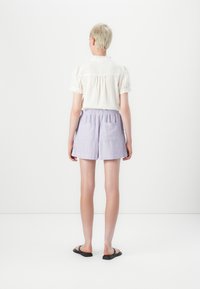 Hvid tekstureret top med korte puffærmer, parret med lyseblå shorts med lodrette lyserøde striber og to sidelommer. Sorte sandaler.