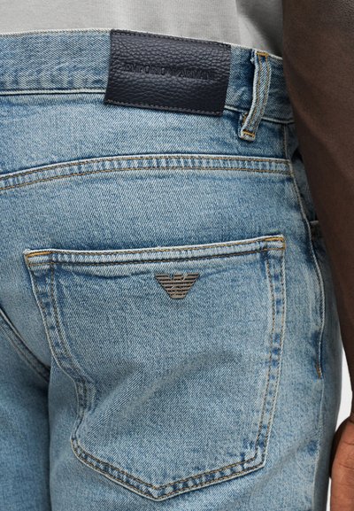 Ανοιχτά μπλε τζιν από denim διαθέτουν ετικέτα από μαύρο δέρμα στη μέση με ανάγλυφο λογότυπο και μεταλλικό διακοσμητικό με λογότυπο στην πίσω τσέπη.