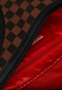 Bag a scacchi marroni e neri parzialmente aperta per rivelare un interno rosso con un portacarte SprayeGar visibile.