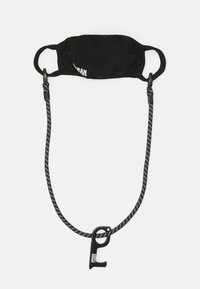 Svart tygmask med elastiska öronloopar och en avtagbar svart och vit prickig rem med en klämma för säker fästning.